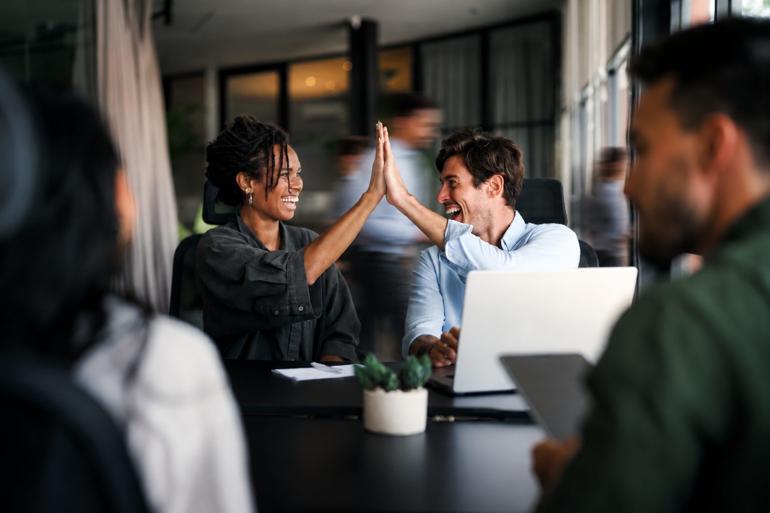 Dois colegas comemorando com um high-five em uma mesa de reunião